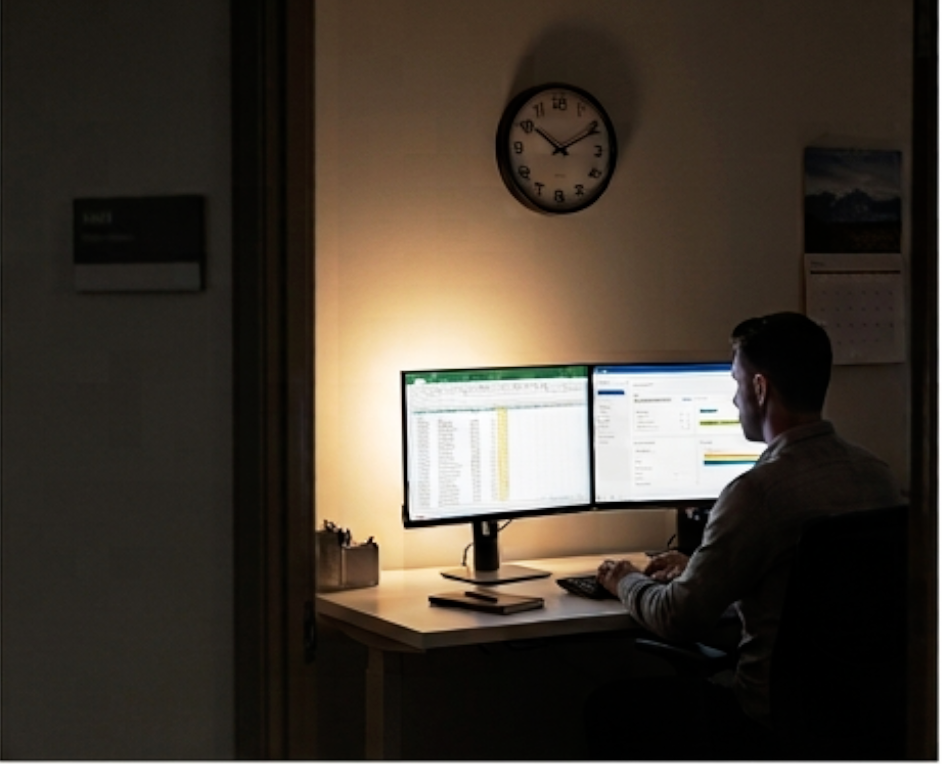 A practitioner working at two monitors in a small office late in the evening